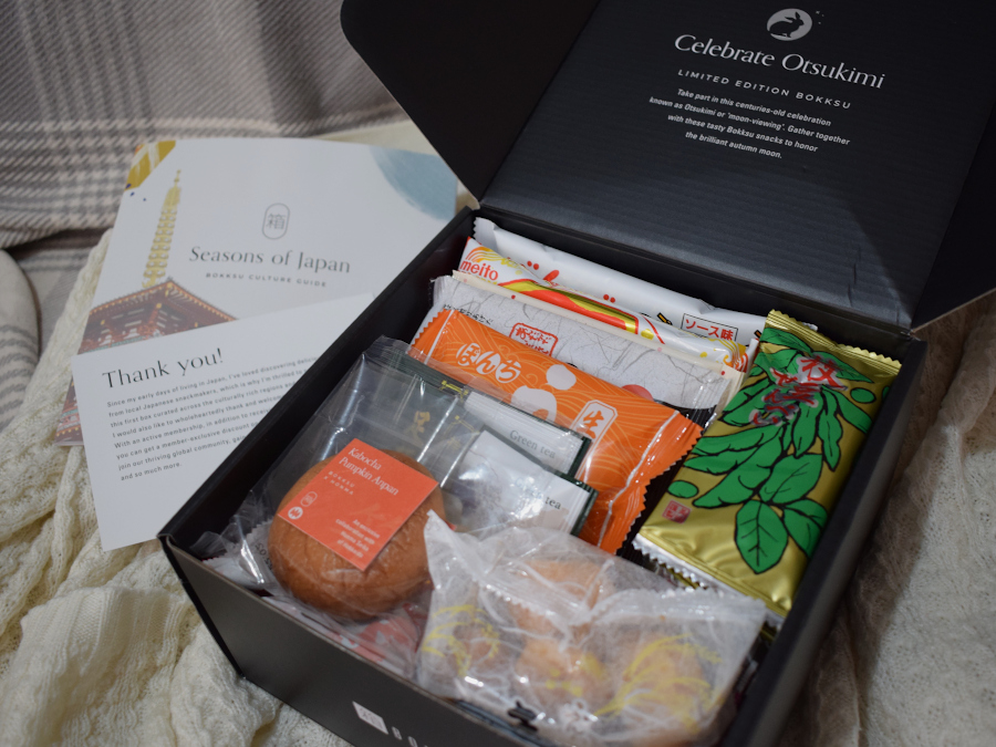 A snack filled cardboard box with a welcome card and booklet of contents