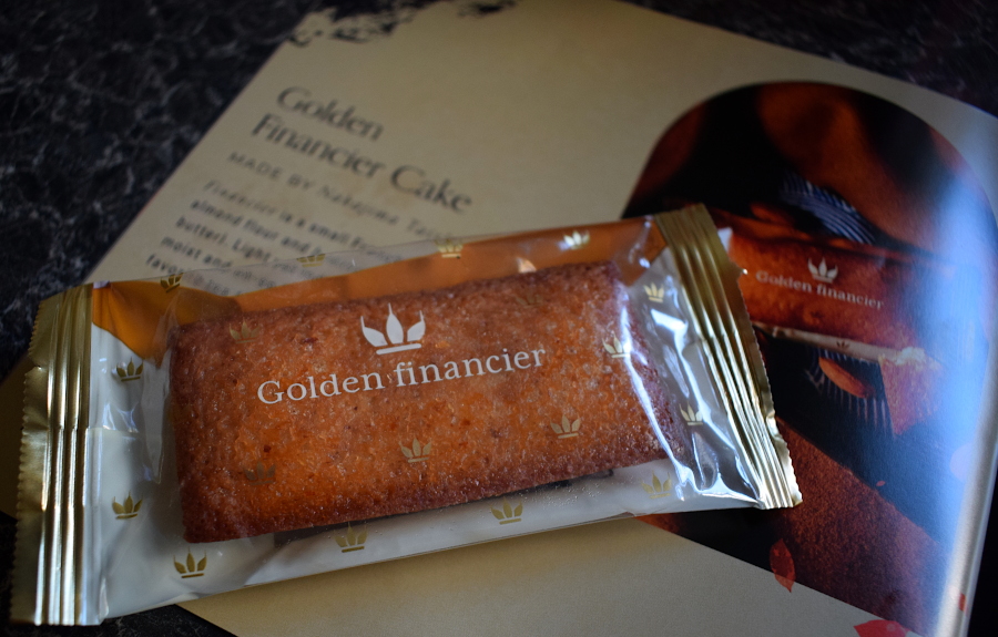 a single golden financier cake slice next to a leaflet describing them