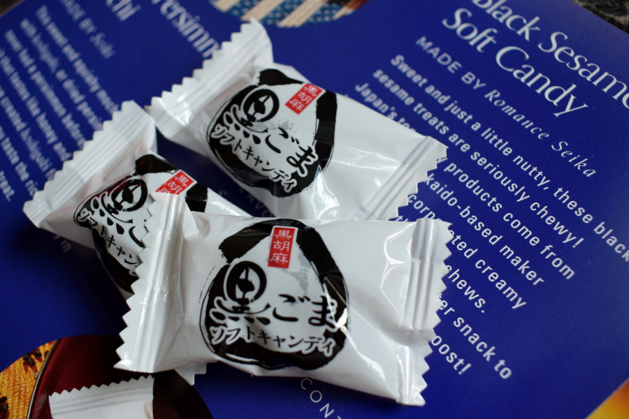 three individually wrapped soft black sesame seed sweets next to a leaflet describing them