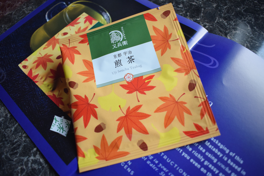 a single wrapped pyramid style uji sencha green tea bag next to a leaflet describing them